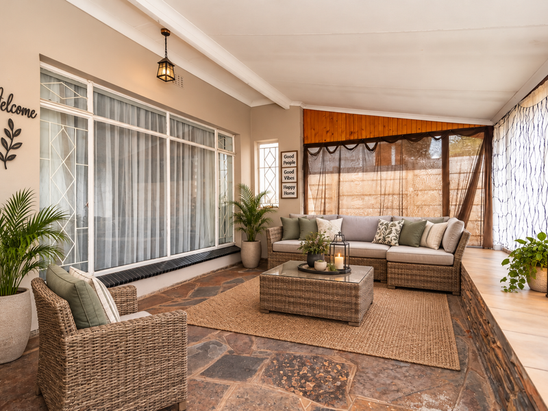 A covered patio area featuring natural stone flooring, timber ceiling accents, and large windows, providing a comfortable and inviting outdoor living space.