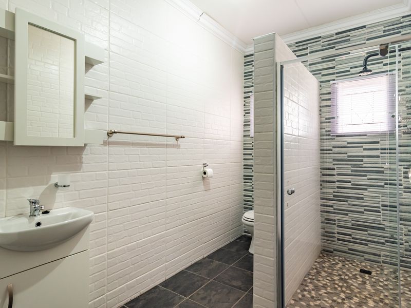 Modern bathroom featuring a walk-in shower with mosaic floor tiles, a vanity unit with integrated mirror, and stylish textured wall tiling.
