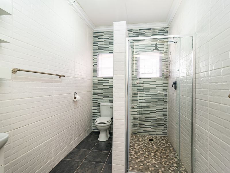 A clean, modern bathroom featuring a glass-enclosed shower with pebble-style flooring, a separate toilet area, and white tiled walls with decorative mosaic accents.