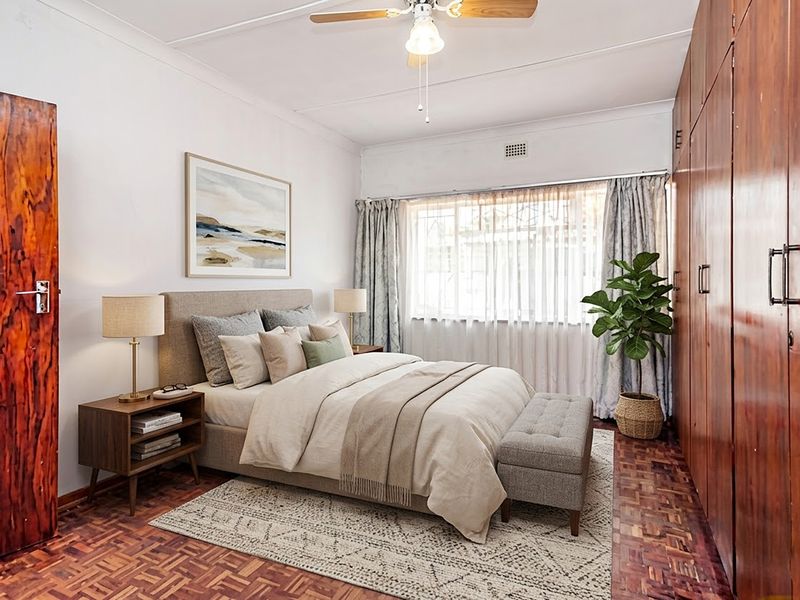 A well-maintained bedroom featuring classic parquet flooring, extensive built-in wooden cabinetry, and a ceiling fan, offering a warm and functional living space.