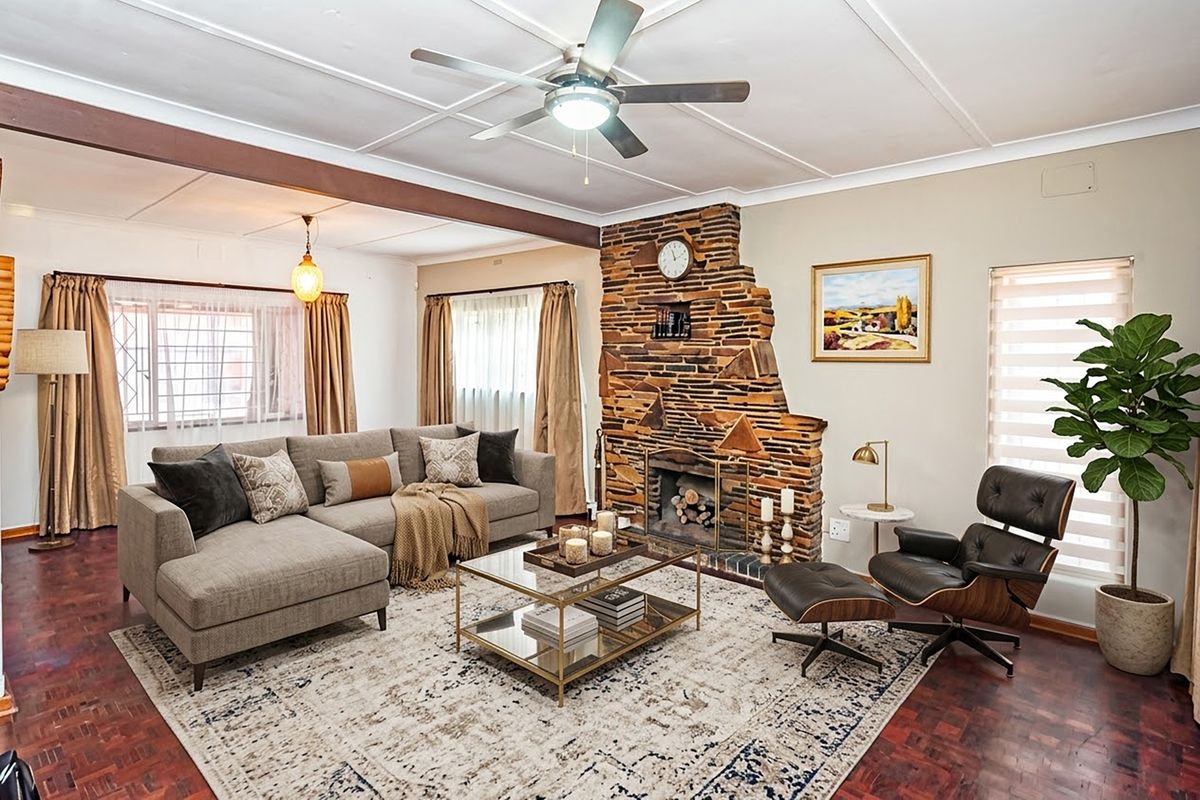 Spacious living room featuring a distinctive stone fireplace, parquet flooring, and an exposed ceiling beam, creating a warm and inviting atmosphere.