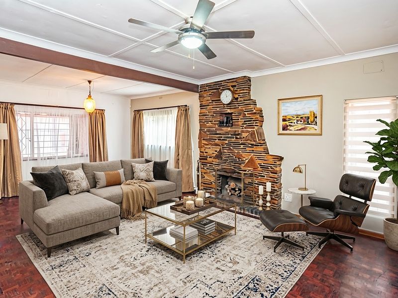 Spacious living room featuring a distinctive stone fireplace, parquet flooring, and an exposed ceiling beam, creating a warm and inviting atmosphere.