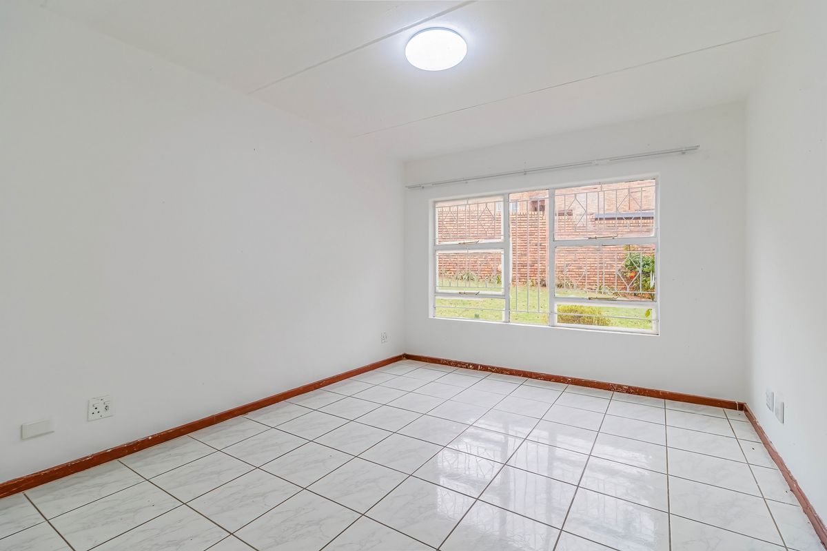 An empty bedroom featuring white walls, tiled flooring, and windows fitted with security bars.