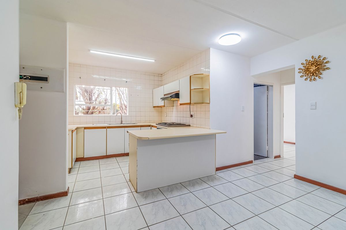 A functional kitchen featuring tiled flooring, a central island, built-in cabinetry, and a gas hob, offering a blank canvas for modern renovation.