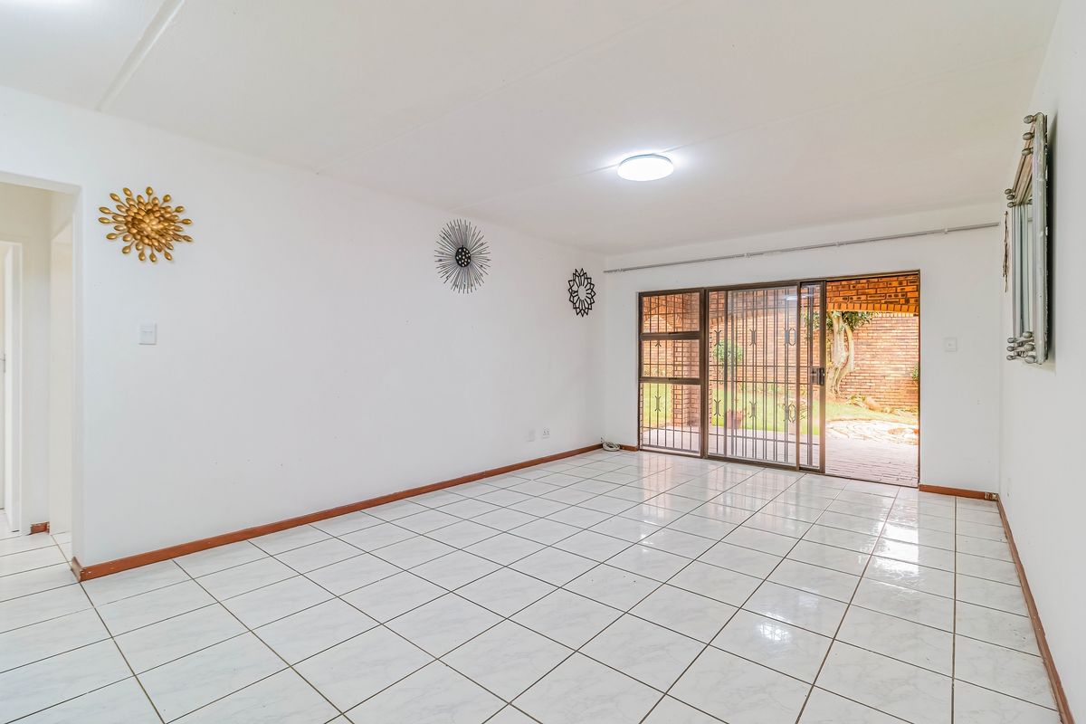 A bright, empty living room featuring white tiled flooring and a sliding glass door with a security gate leading to the rear garden.