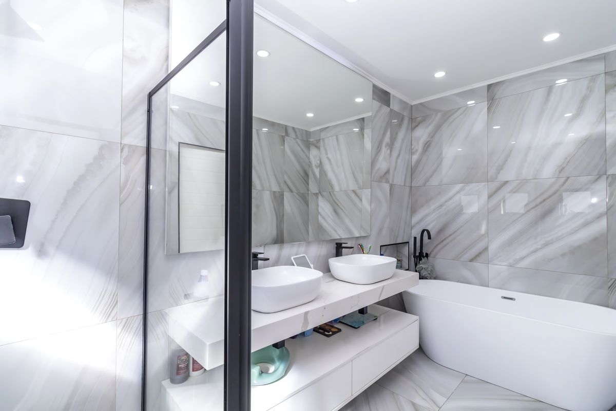 Modern bathroom featuring a double vanity with vessel sinks, a freestanding bathtub, and floor-to-ceiling marble-style wall tiling with black frame accents.