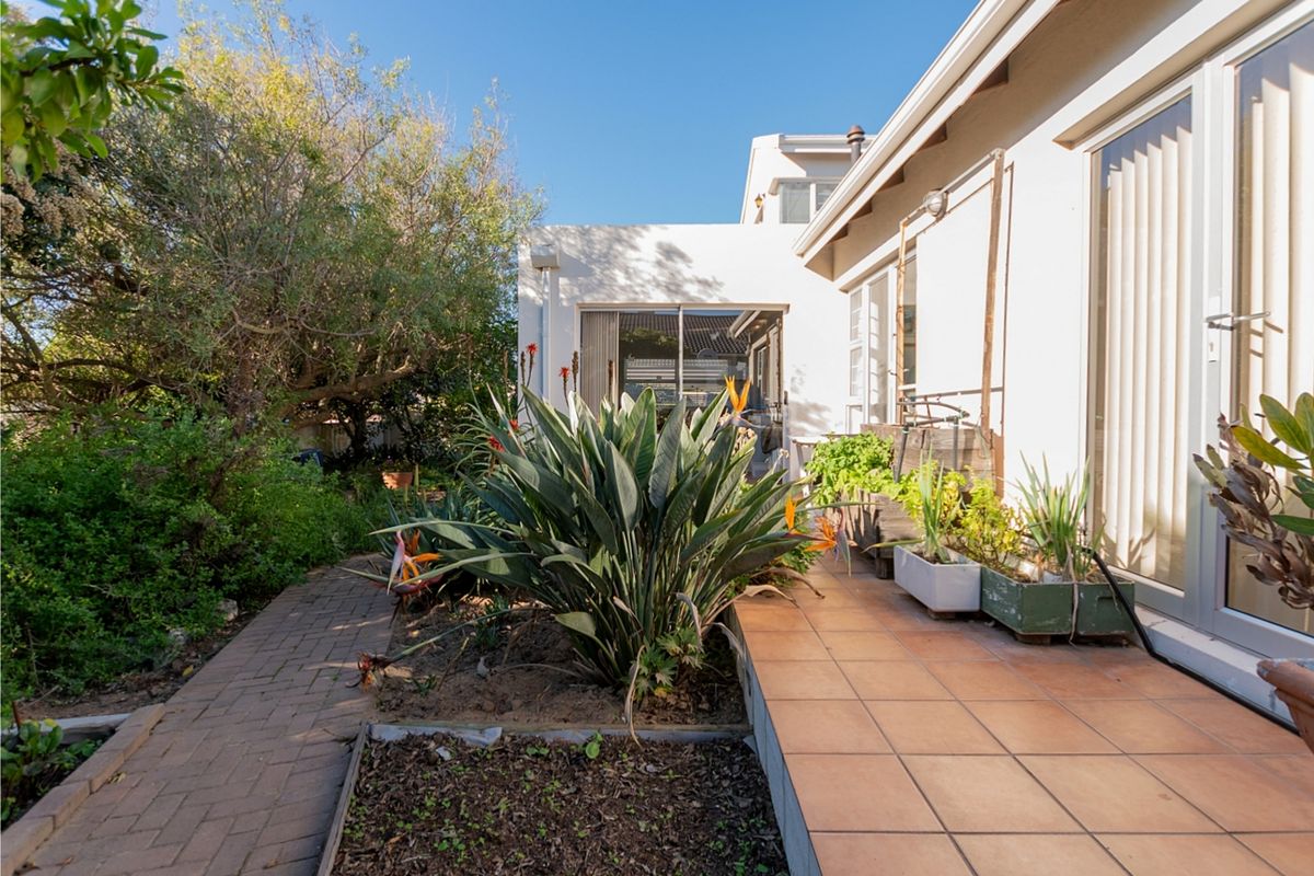 A rear exterior view featuring a tiled patio area, brick pathway, and established garden beds adjacent to the home's sliding glass doors.