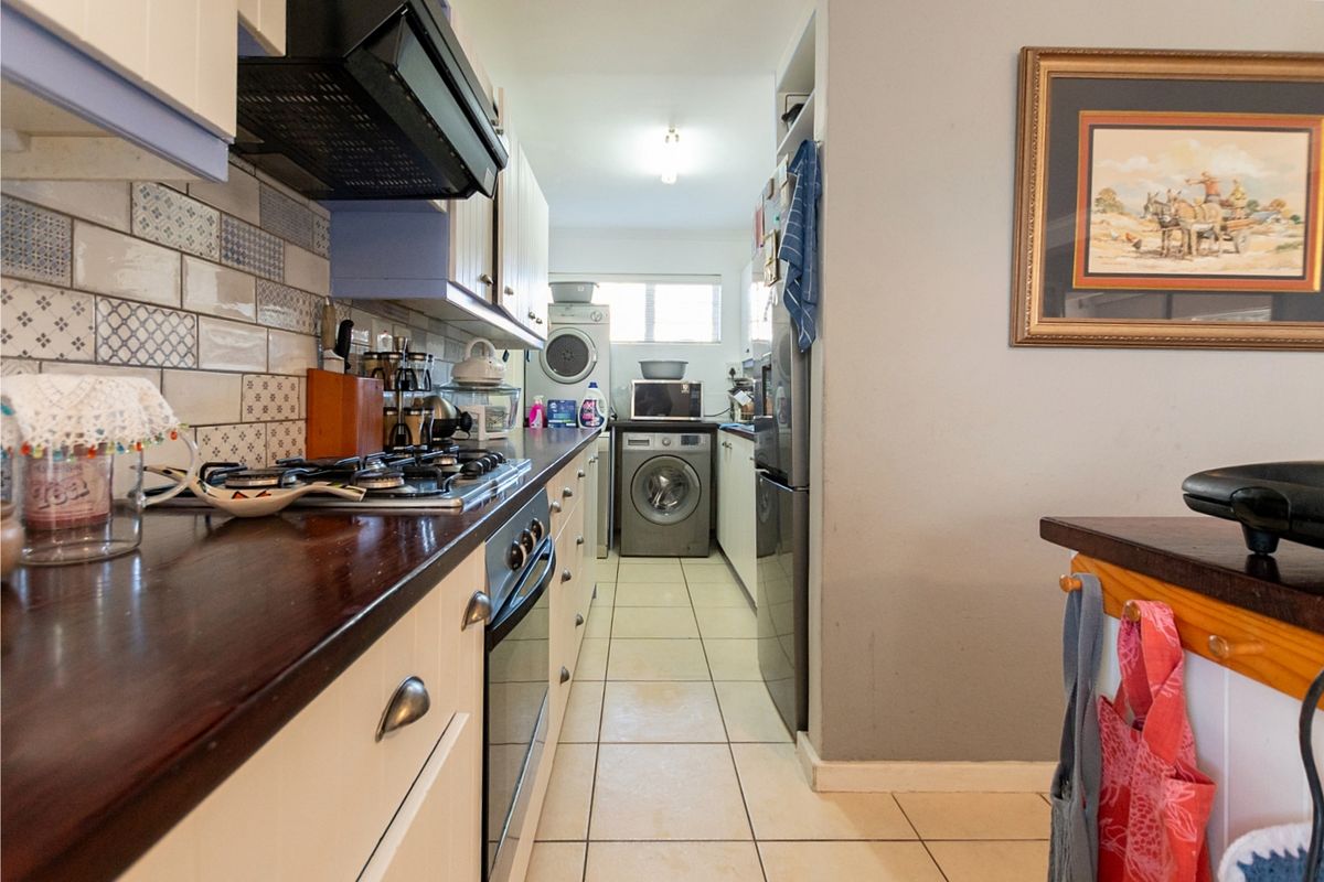 A functional galley-style kitchen featuring built-in cabinetry, a gas hob, integrated oven, extractor fan, and a dedicated laundry area with tiled flooring.