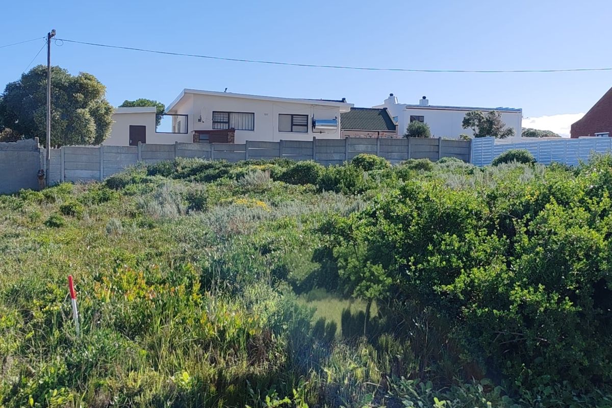 A view of a vacant residential plot featuring native vegetation and a precast concrete boundary wall, with neighboring properties visible in the background.