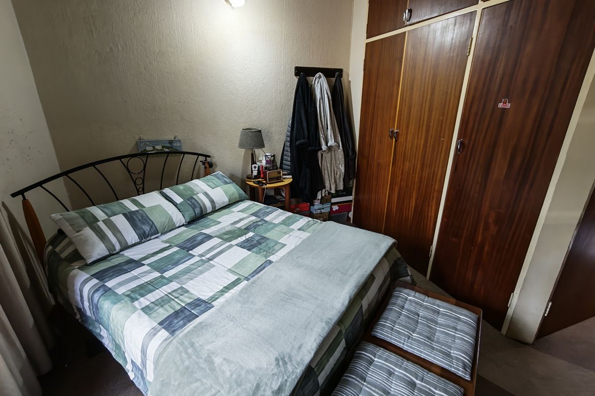 A functional bedroom featuring built-in wooden cupboards and a wall-mounted light fixture, offering a standard layout with potential for cosmetic updates.