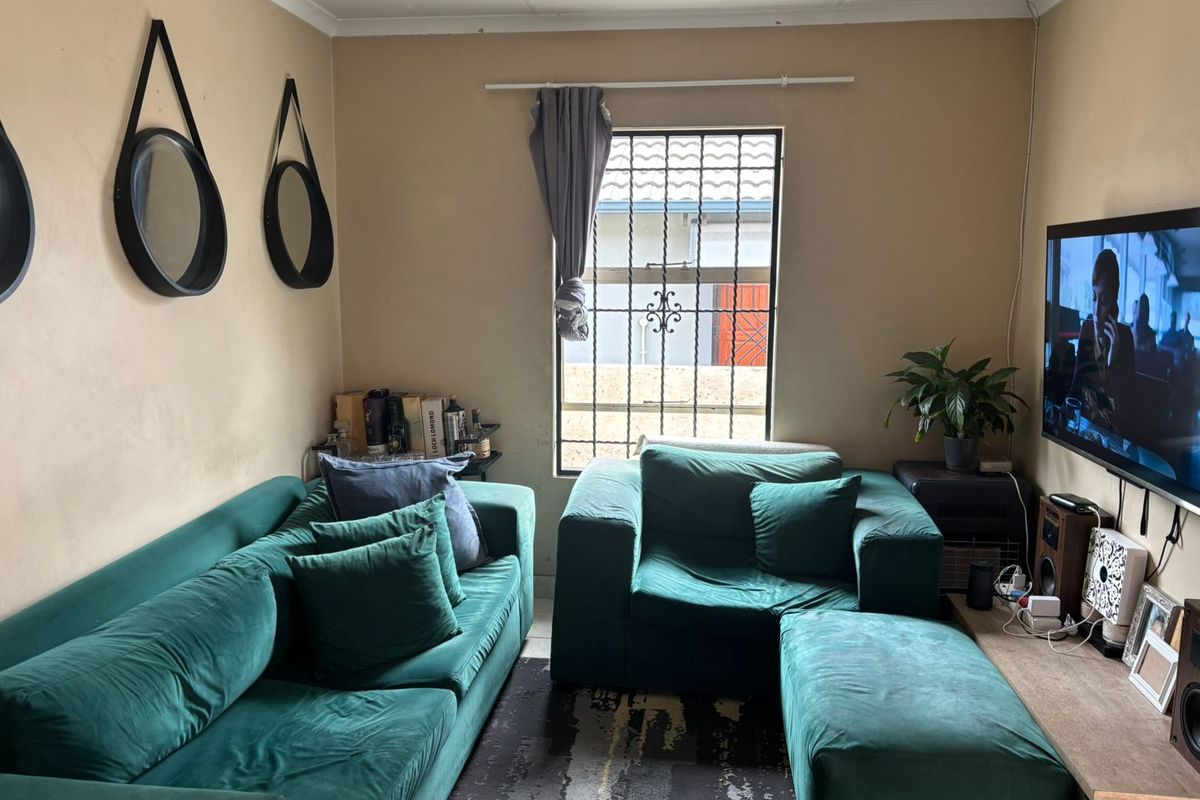 A living room featuring security bars on the window and decorative coving, currently showing signs of wear on the wall surfaces.