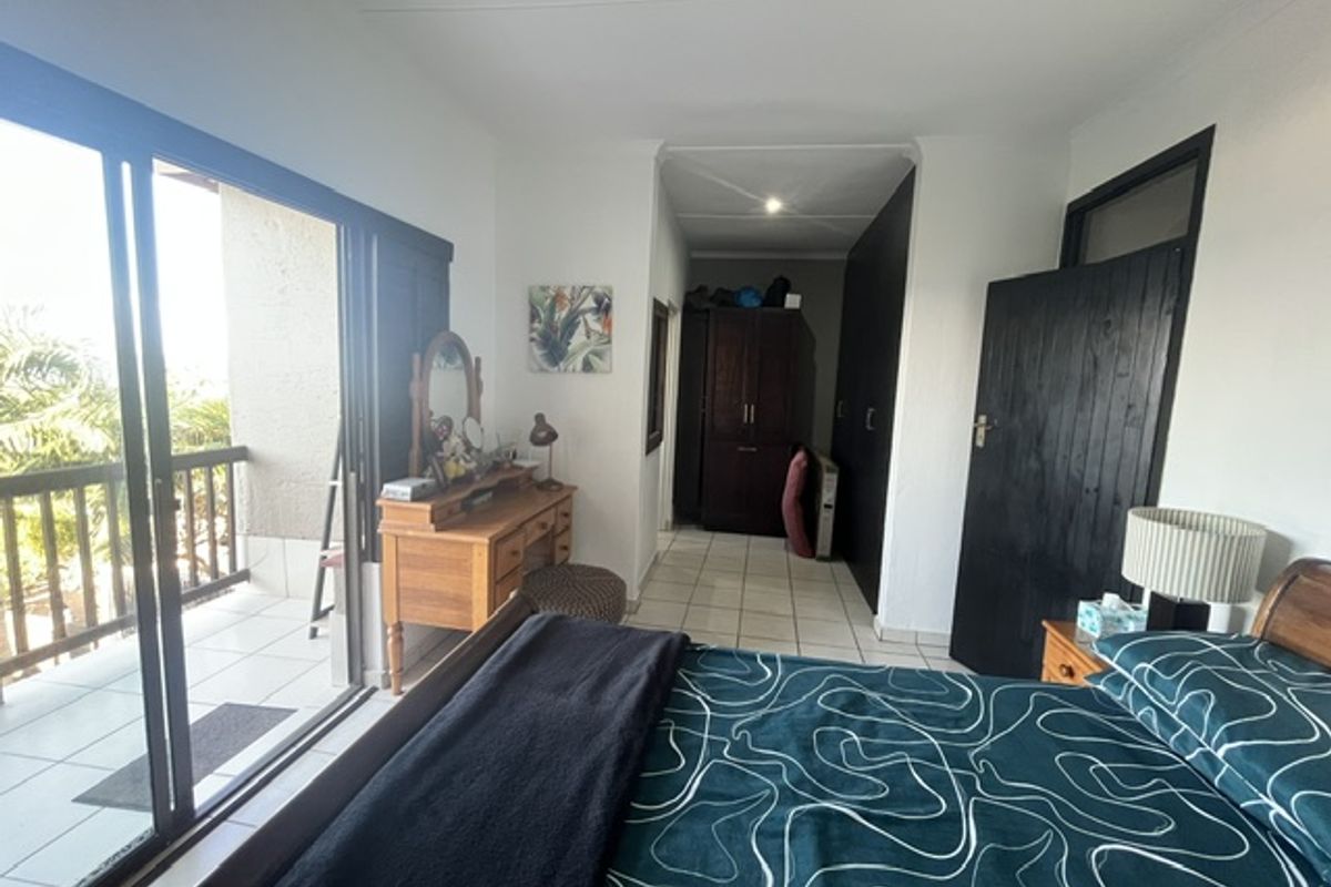 Spacious bedroom featuring tiled flooring, built-in cupboards, and large sliding glass doors providing access to an outdoor balcony area.