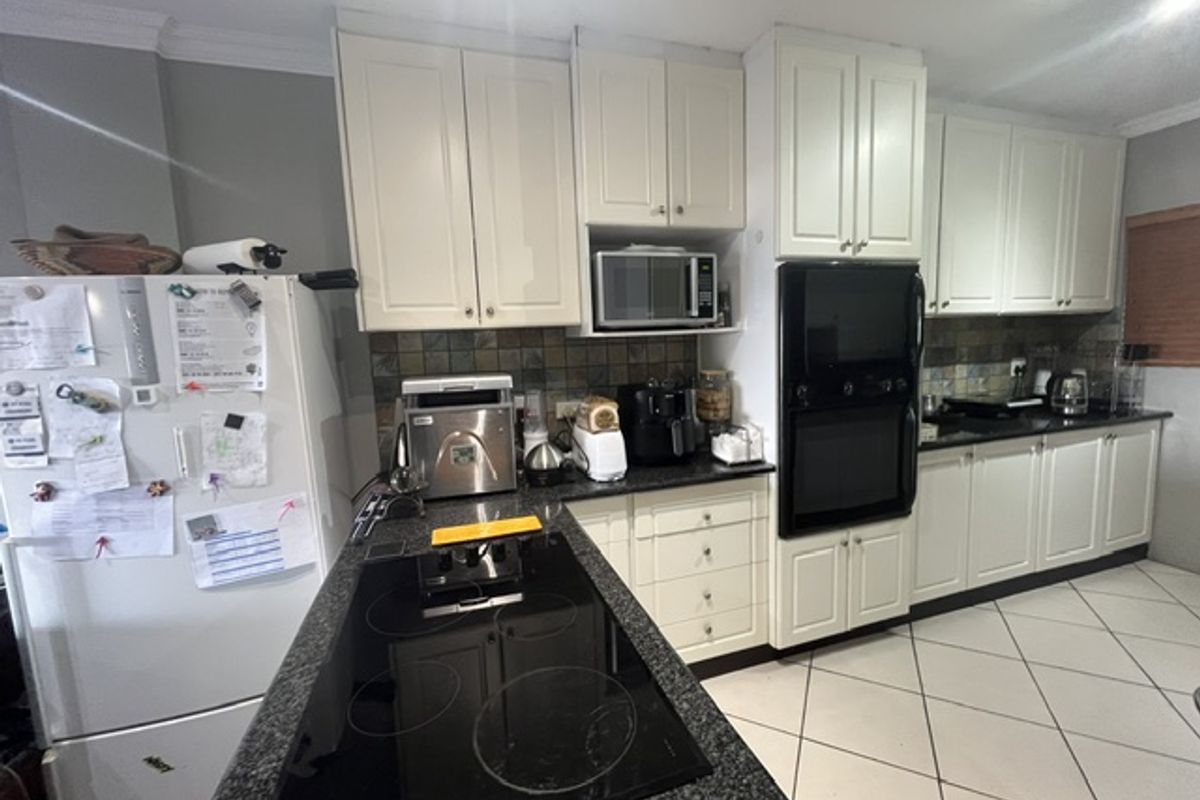 A functional kitchen featuring white cabinetry, granite countertops, a built-in oven, microwave, and an electric hob set within a tiled workspace.