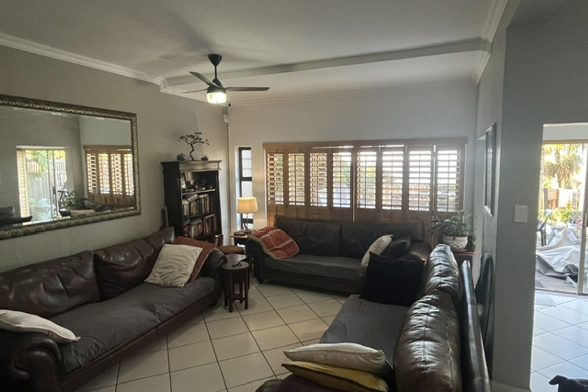 Spacious living room featuring tiled flooring, ceiling fan, and wooden plantation shutters, providing a comfortable and functional lounge area.