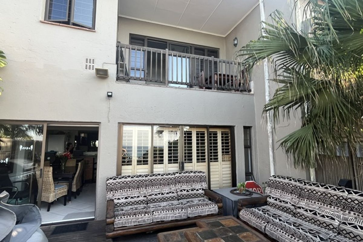 Rear exterior view of the townhouse featuring a wooden deck, covered patio area, and an upper-level balcony with sliding door access.