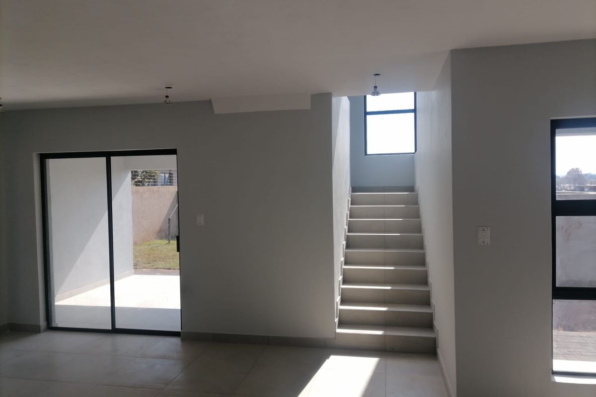 A bright, modern open-plan living area featuring tiled flooring, a staircase, and large sliding glass doors leading to an outdoor patio space.