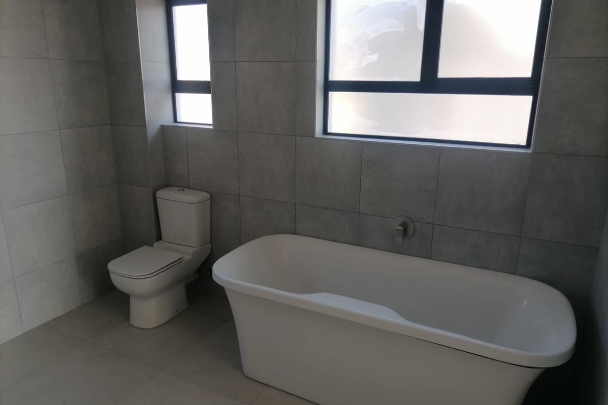 A modern bathroom featuring a freestanding bathtub, a wall-mounted faucet, and a toilet, finished with neutral grey wall and floor tiles.