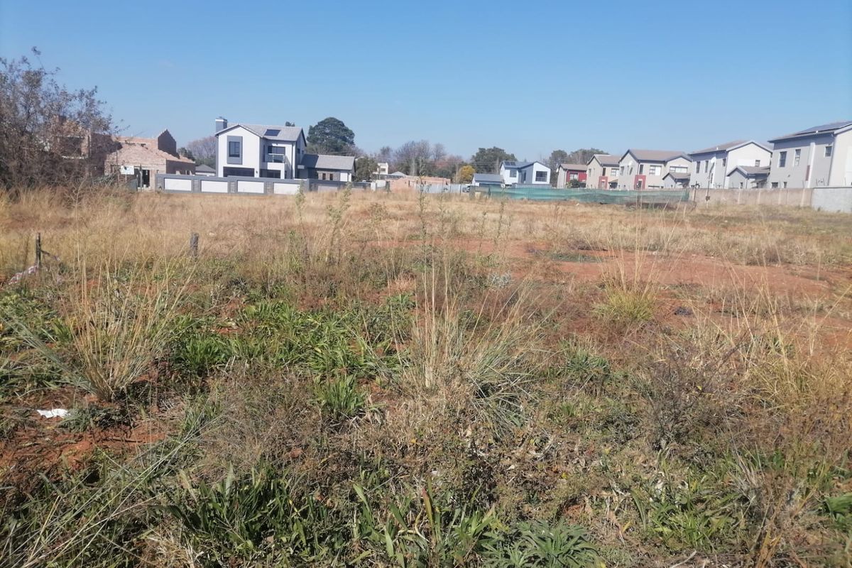 A vacant residential plot of land featuring natural vegetation, situated within an established neighborhood with surrounding residential properties.