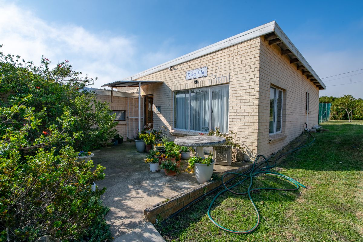 Rear view of a single-story brick house featuring a concrete patio area and established garden surroundings.