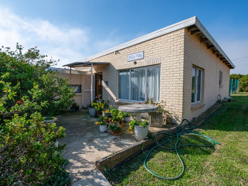 Rear view of a single-story brick house featuring a concrete patio area and established garden surroundings.