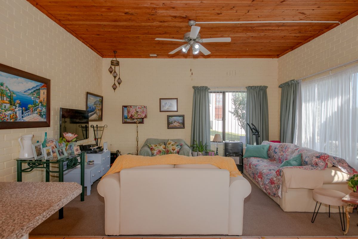 A living room featuring a warm exposed timber ceiling, painted brick walls, and large windows fitted with security bars.