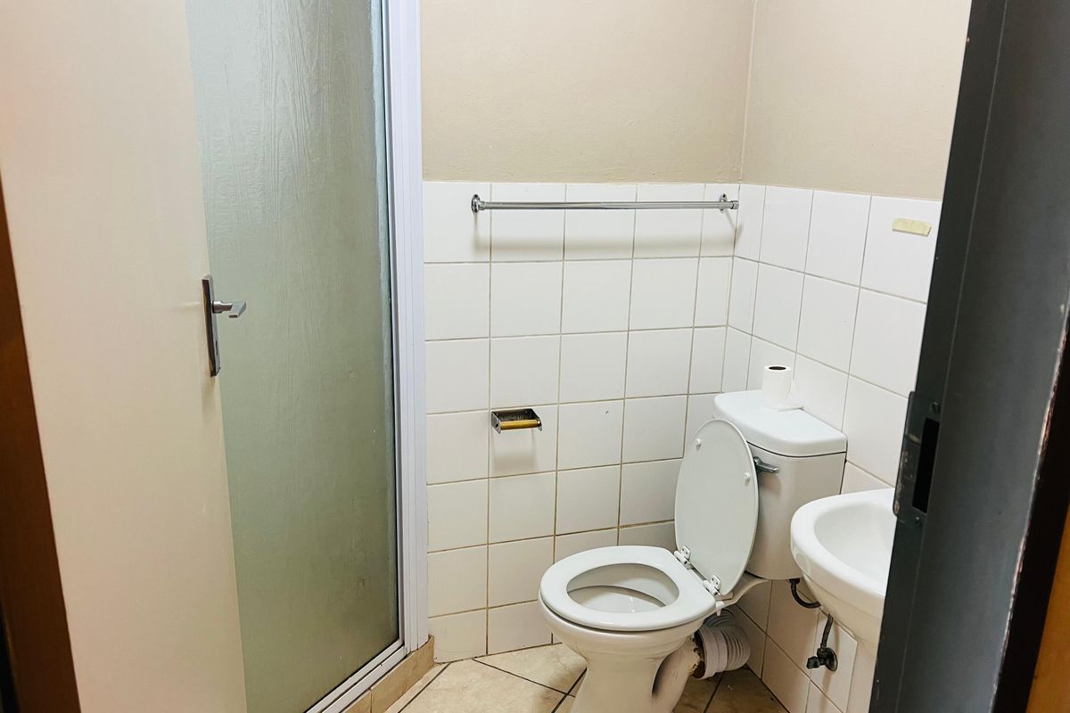A compact bathroom featuring a white toilet, pedestal basin, and a shower enclosure with a frosted glass door.