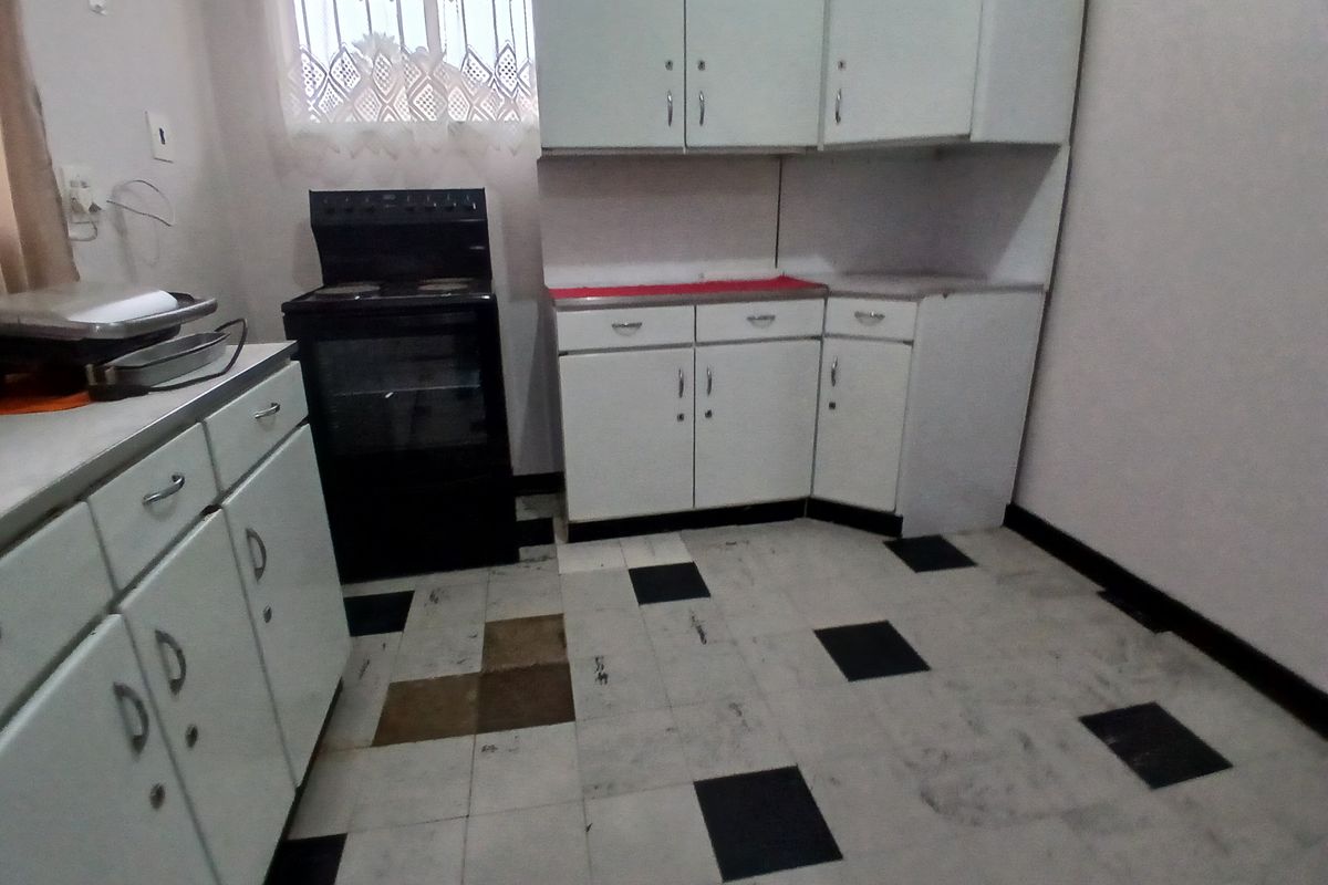 A dated kitchen featuring white built-in cabinetry, a black freestanding stove, and a checkered tile floor in need of refurbishment.