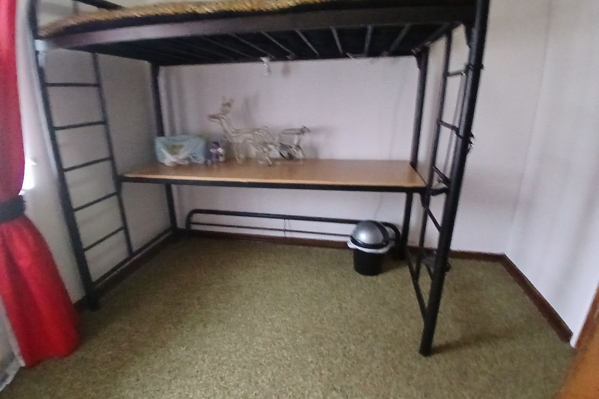 A bedroom space featuring a metal loft bed frame with an integrated desk area and carpeted flooring.