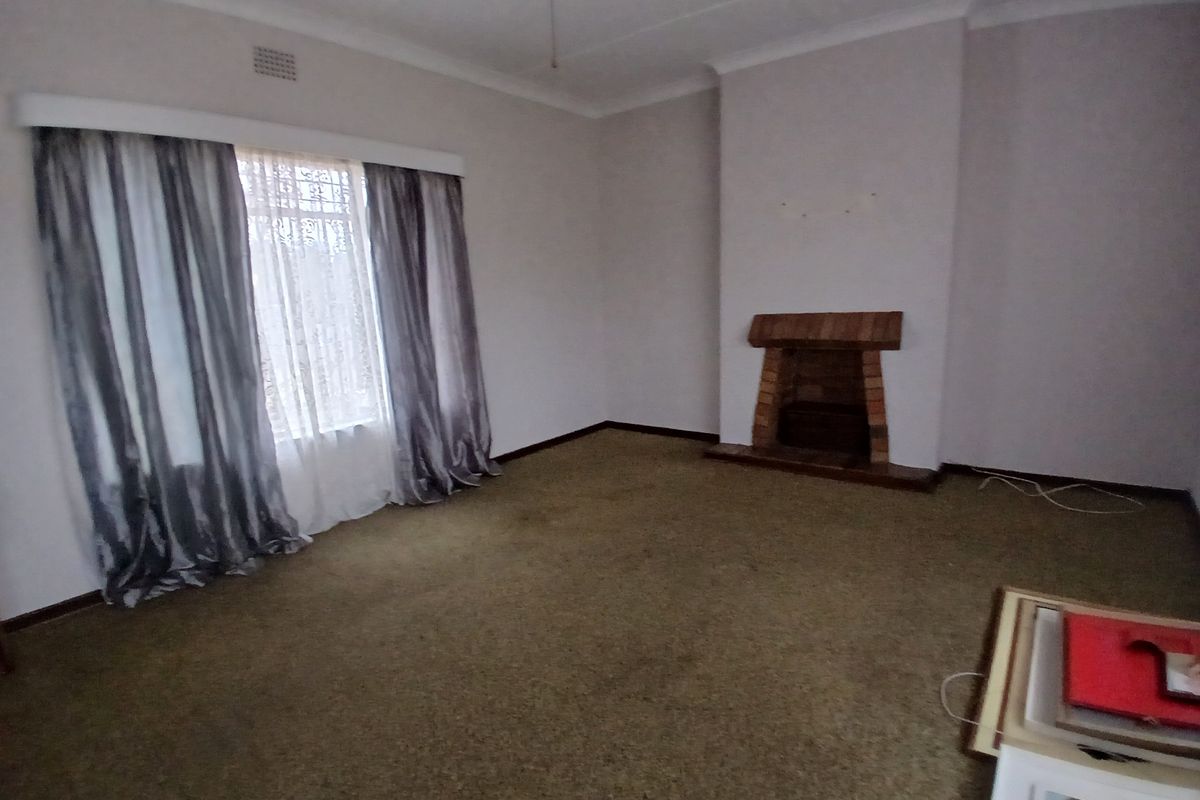 A spacious, empty living room featuring a traditional brick fireplace and carpeted flooring, offering a blank canvas for renovation and interior design updates.