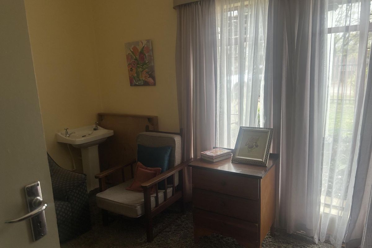 A bedroom featuring a built-in pedestal basin, carpeted flooring, and large windows with curtain tracks, offering a functional space with potential for modernization.
