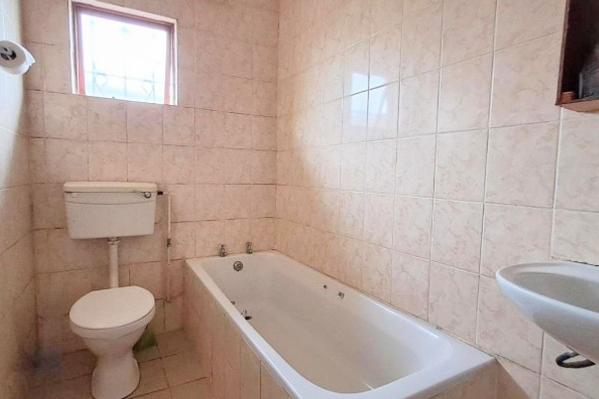 A functional bathroom featuring a standard bathtub, pedestal basin, and toilet with dated wall tiling throughout.