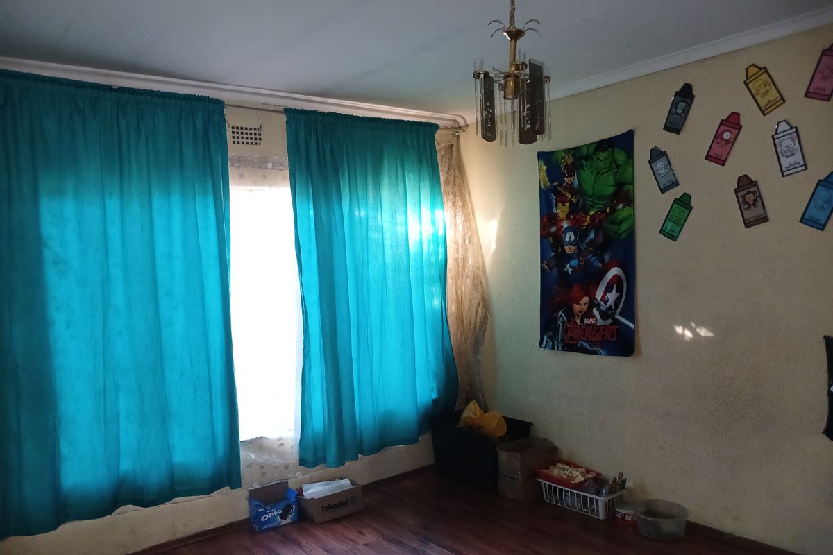 A bedroom featuring laminate flooring, a central light fixture, and large windows covered by curtains.