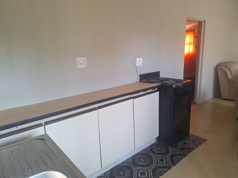 A functional kitchen area featuring built-in cabinetry, a stainless steel sink, and a freestanding electric stove with tiled flooring.