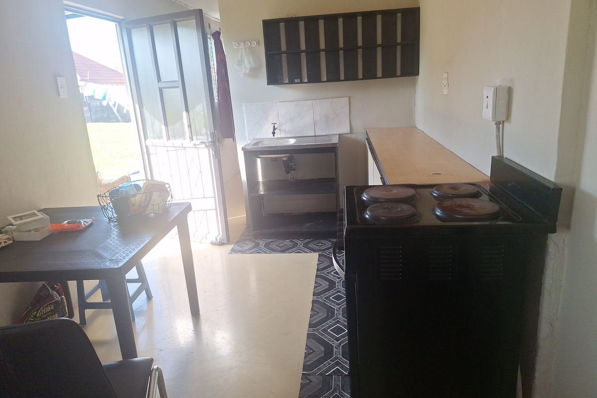 A functional kitchen area featuring a basic sink, electric stove, and wall-mounted shelving with direct access to the exterior via a security gate.