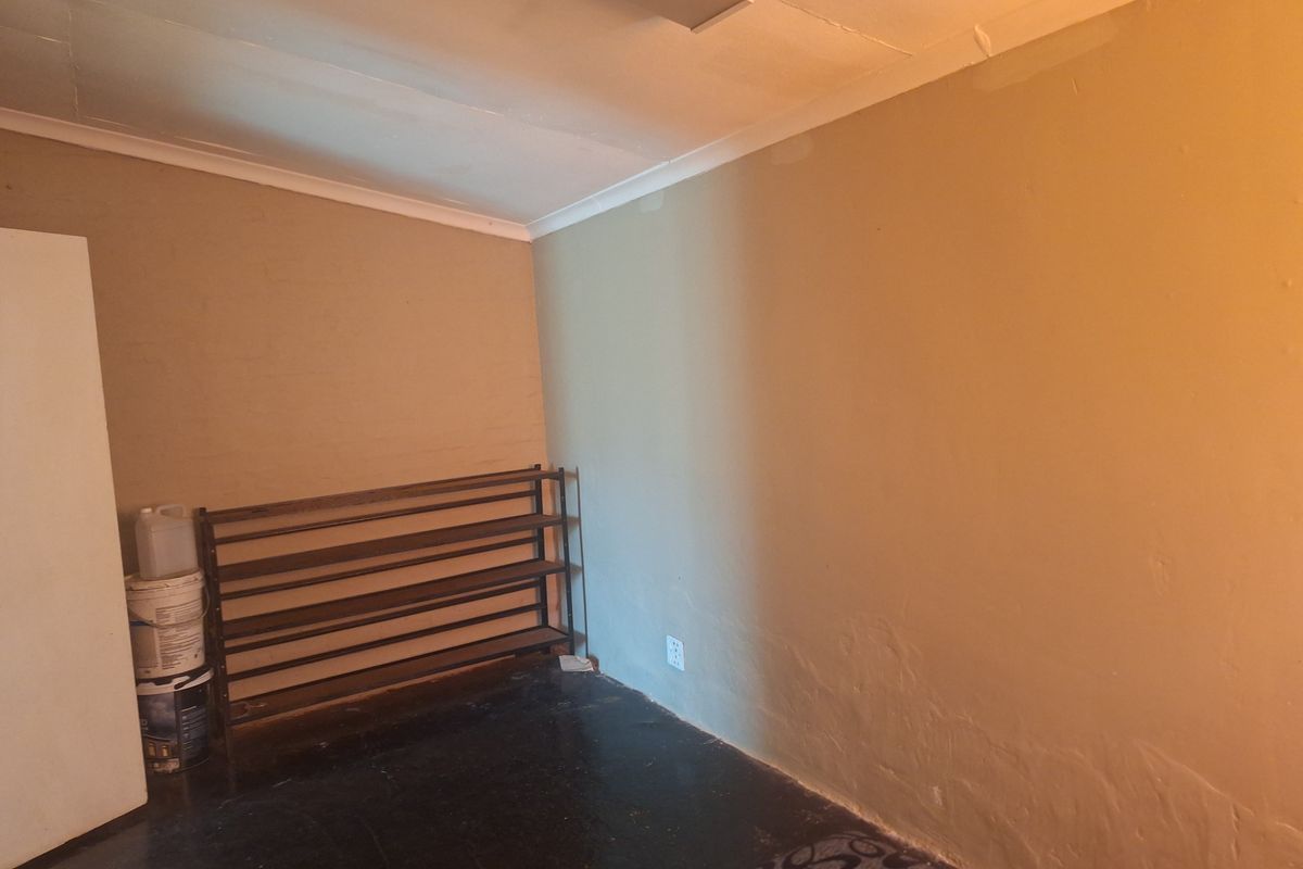 An empty bedroom featuring a simple layout with cove cornicing, a fluorescent light fixture, and dark flooring, offering a blank canvas for renovation.