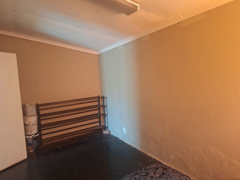 An empty bedroom featuring a simple layout with cove cornicing, a fluorescent light fixture, and dark flooring, offering a blank canvas for renovation.