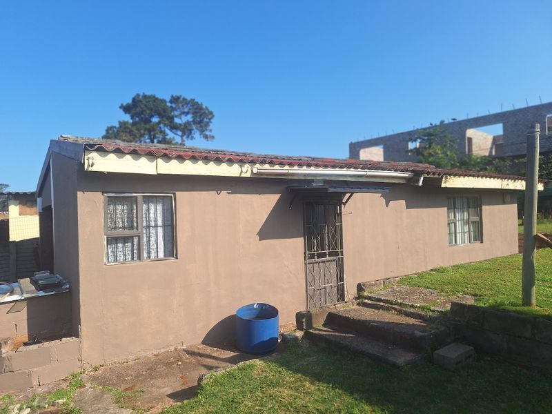 Rear exterior view of a single-story house featuring a tiled roof, security gate, and concrete steps leading to the entrance.