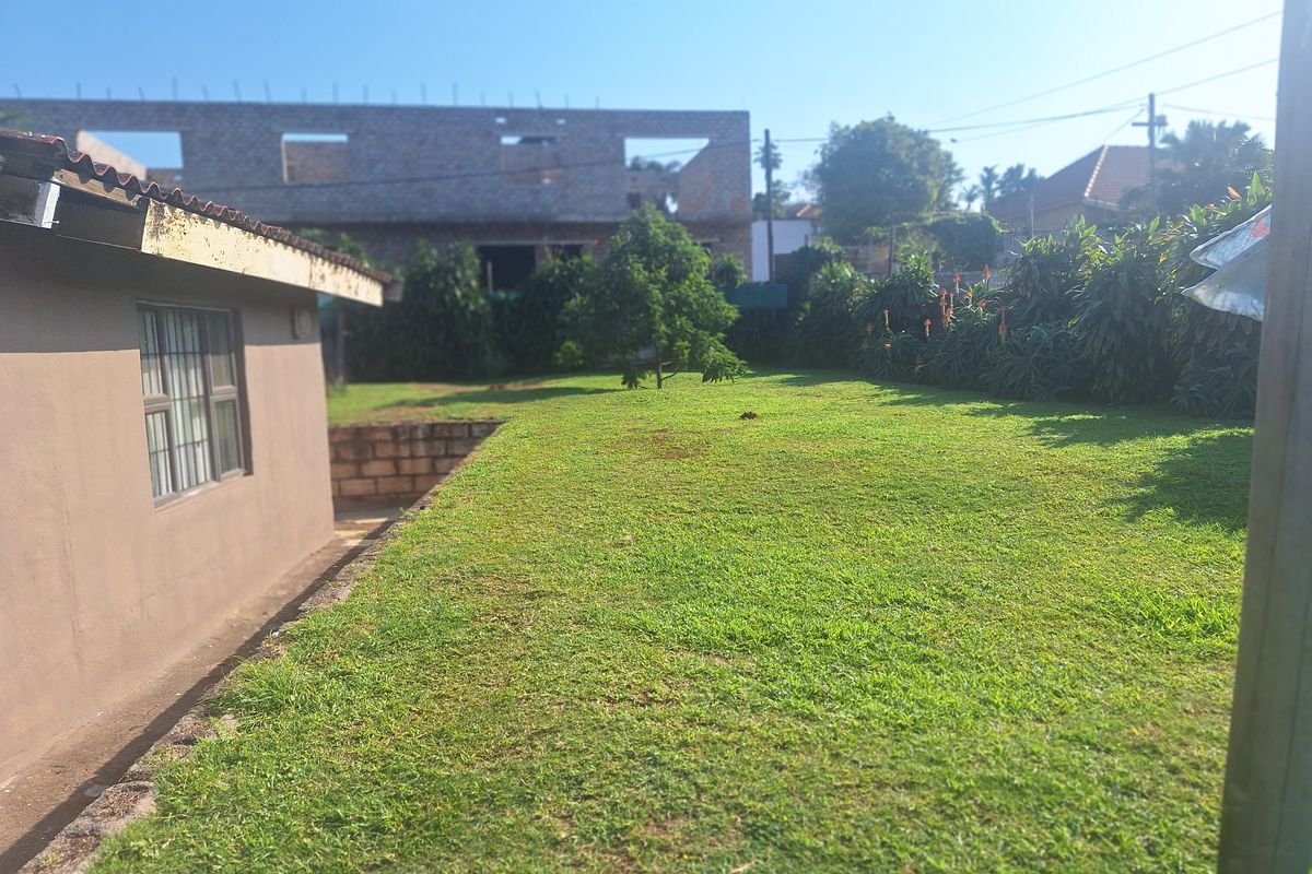 A view of the rear garden featuring a lawn area, retaining wall, and the side elevation of the house with security bars on the windows.