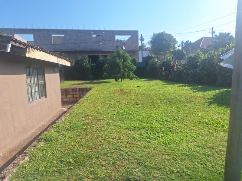 A view of the rear garden featuring a lawn area, retaining wall, and the side elevation of the house with security bars on the windows.