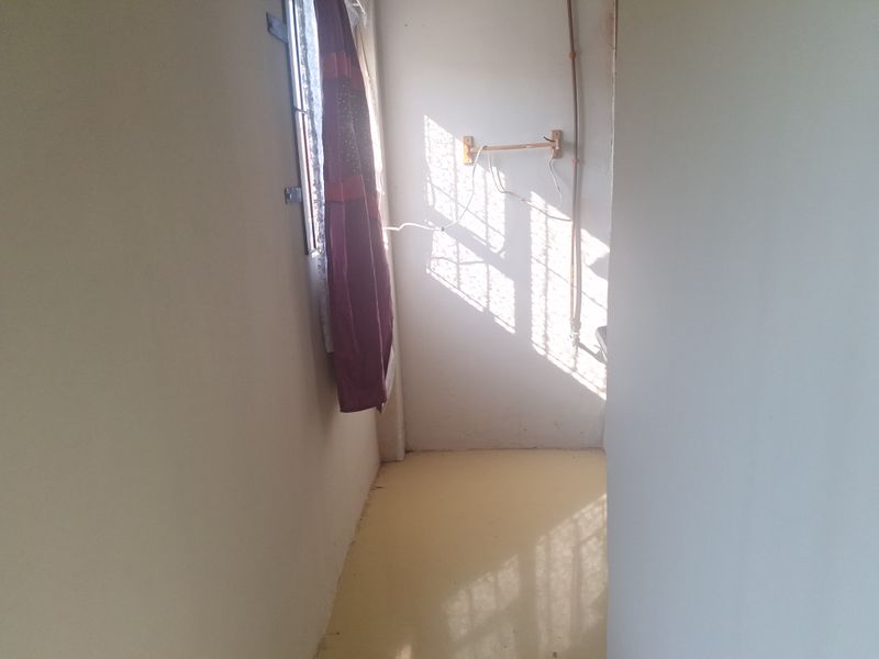 A small, empty utility space featuring a window and exposed wall piping, requiring cosmetic updates and electrical safety improvements.