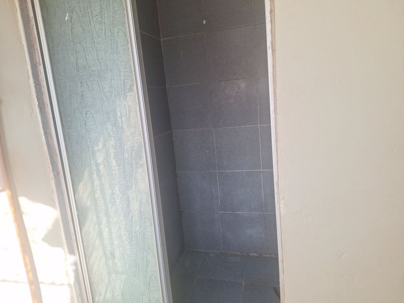 A small shower cubicle featuring grey wall and floor tiles, currently requiring maintenance to the shower door frame and surrounding wall finishes.