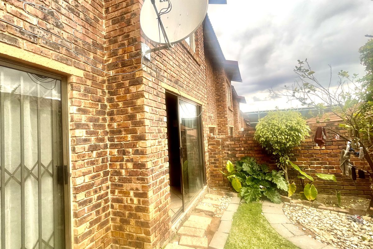 Rear exterior view of the apartment featuring face brick walls, sliding glass doors with security gates, and a small private garden area.