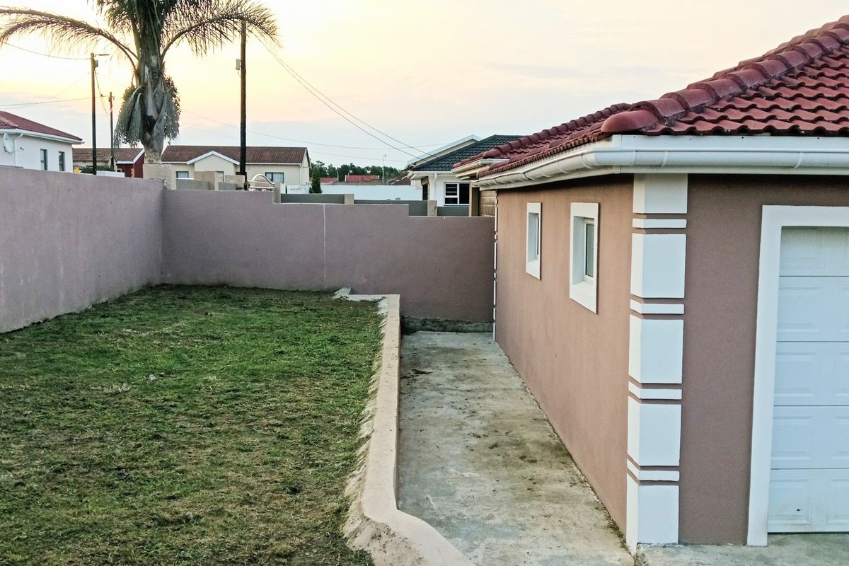 Rear exterior view of the property featuring a concrete pathway, boundary wall, and access to the garage.