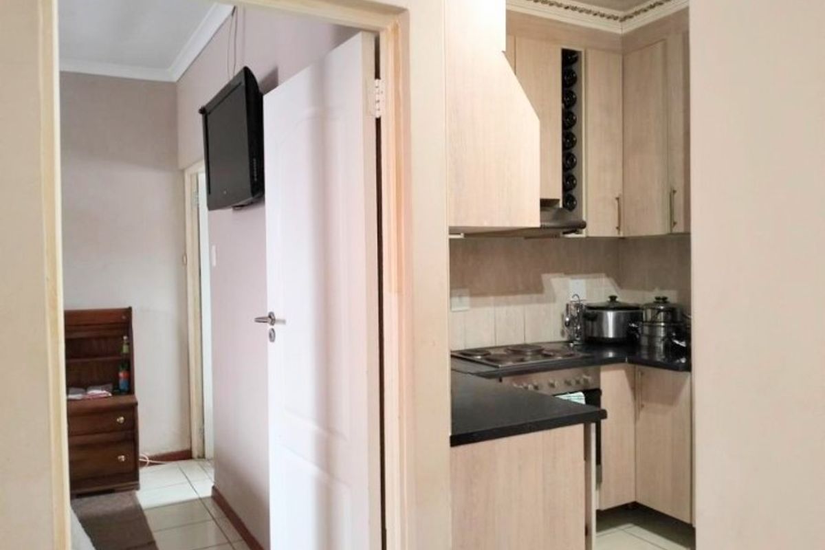 A compact kitchen featuring light wood-finish cabinetry, dark countertops, and integrated appliances, viewed from an adjacent hallway.