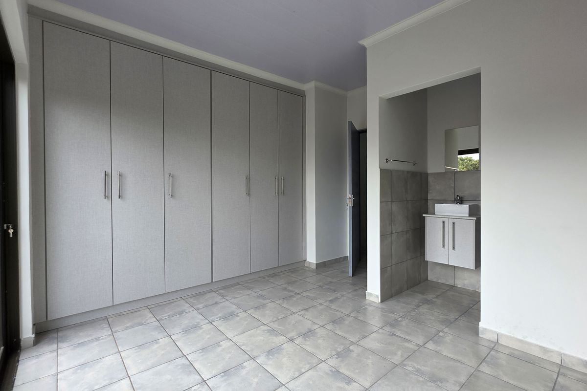 Spacious bedroom featuring extensive built-in cupboards and an integrated vanity area with a modern basin and tiled splashback.