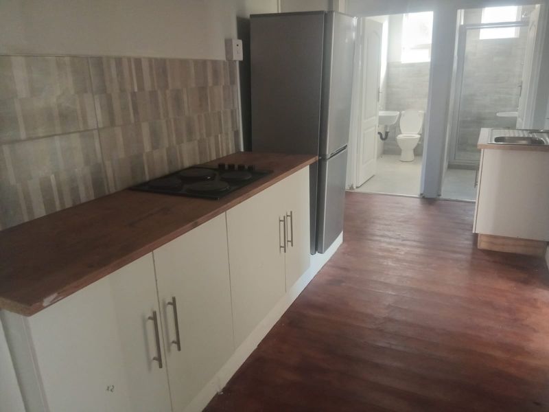Compact kitchen area featuring built-in cabinetry, a hob, and a tiled backsplash, with direct access to an adjacent bathroom.
