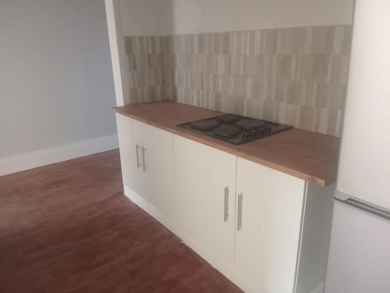 A compact kitchen area featuring modern white cabinetry, a wooden countertop, and a built-in electric hob with a neutral tiled backsplash.