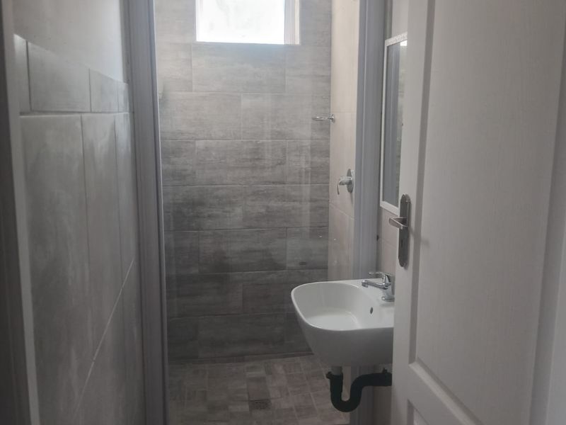 A compact bathroom featuring a shower enclosure, wall-mounted basin, and modern grey tiling throughout.
