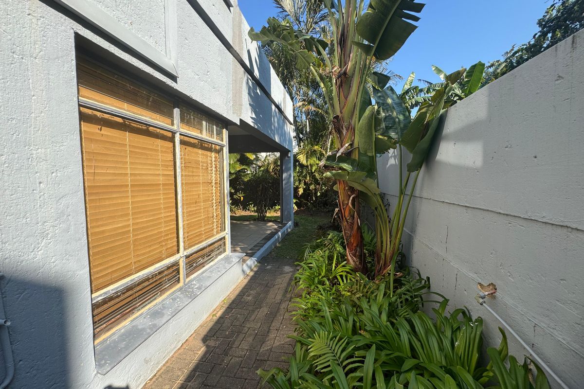 A side walkway featuring paved flooring, a boundary wall with exposed wiring, and access to a covered patio area.