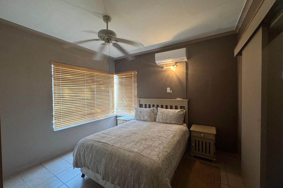 A functional bedroom featuring tiled flooring, a ceiling fan, split-system air conditioning, and venetian blinds for privacy.